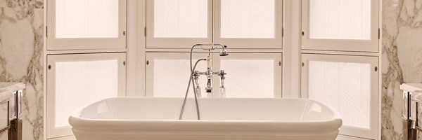 Luxurious marble bathroom featuring a freestanding white tub, classic chrome taps, and tall frosted windows.