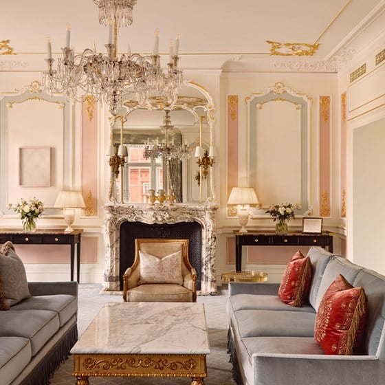 Regal lounge with twin sofas, marble coffee table, ornate fireplace and mirrors, crowned by crystal chandeliers.