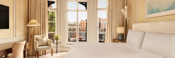 Elegant bedroom with king-size bed, cream armchair, and French doors leading to a private terrace with wrought iron railing and Mayfair views.