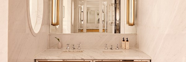 Luxurious marble bathroom with double vanity, backlit mirrors, chrome fittings, and Claridge’s branded toiletries neatly arranged on the counter.