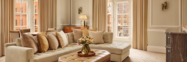 Spacious lounge and dining area with neutral tones, soft corner sofa, wood-panelled furniture, and floor-to-ceiling windows bringing in natural light.