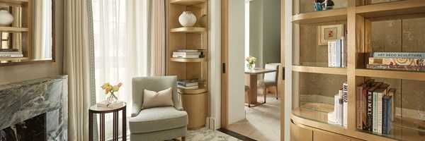 Elegant reading nook with marble fireplace, armchair, floor-to-ceiling shelves, and a view into the dining area beyond sliding doors.
