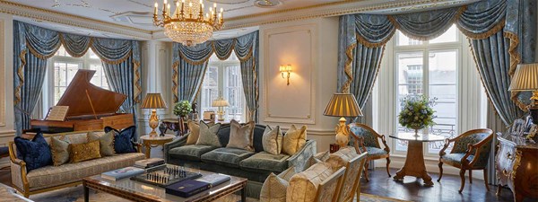 Royal Suite at Claridge's - lounge area with sofa, coffee table with chess game and books on top, grand piano next to the window and blue curtains with patterns on the windows.
