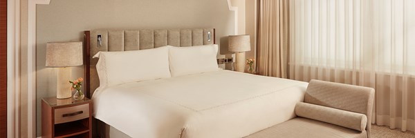 Bedside detail in Superior Room 131, featuring a textured headboard, wooden side table with glass top, ceramic lamp, and small floral arrangement.