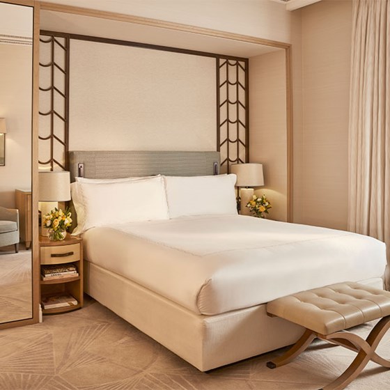 Superior Room at Claridge’s featuring a cream upholstered bed with patterned carpet, bedside tables with matching lamps and floral arrangements, and soft lighting in a neutral palette.