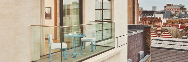 A private terrace with blue bistro-style table and chairs overlooking the rooftops of London, with glass balustrades and access from the bedroom.