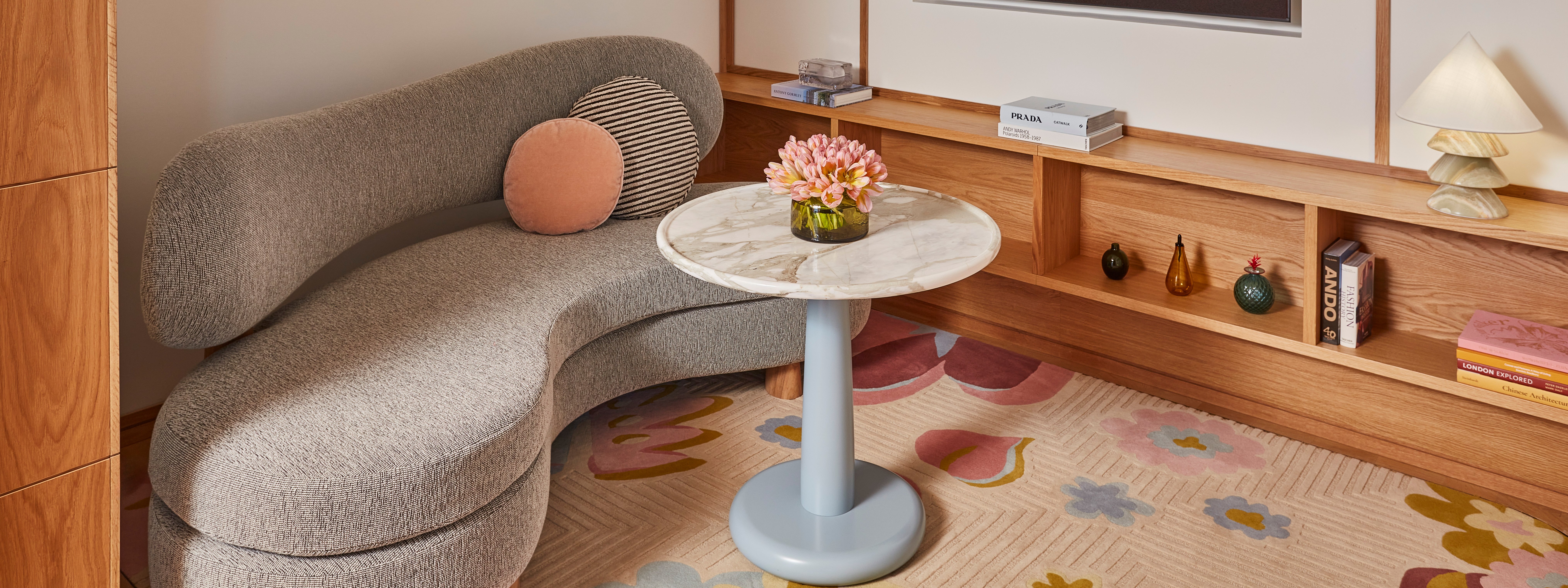 Claridges BOS Terrace Junior suite sitting area. A couch sits to the left and a circular marble table with flowers sits in front of it. A TV sits in the background.