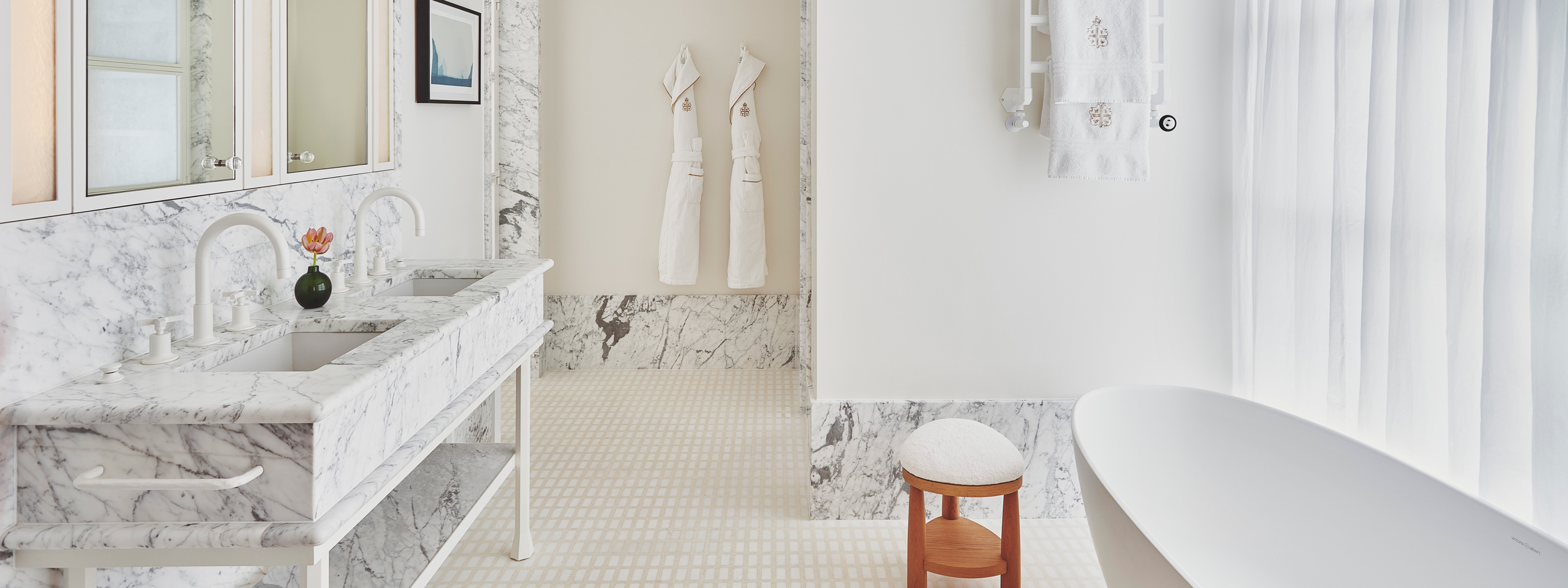 Claridges BOS Terrace Junior suite bathroom. A window is to the right and a bath sits in front of it. Two marble sinks are to the left. Two mirrors sit above the sinks.