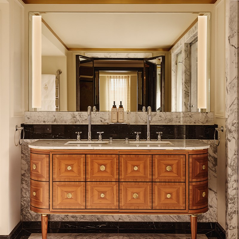 Luxurious twin vanity with inlaid wood drawers, marble countertop, and wide mirror flanked by vertical lights.