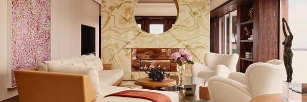 Elegant living room features curved fireplace with marble surround, plush seating, bronze sculpture, and floral accents against modern decor.