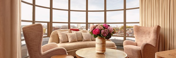 Intimate seating nook with curved sofa, two armchairs, and large round window offering panoramic city views through soft beige curtains.