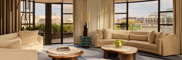 Elegant curved living room with neutral-toned sofas, marble coffee tables, and floor-to-ceiling windows overlooking a landscaped terrace.