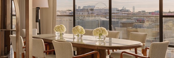 Sophisticated dining room with long marble table, cream-upholstered chairs, and glass walls framing city views and soft natural light.