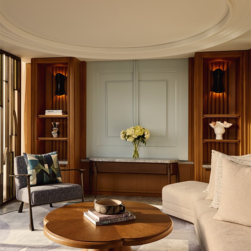 Intimate seating nook with round coffee table, sculptural decor, built-in wood shelving, and soft lighting surrounding a pale blue wall panel.