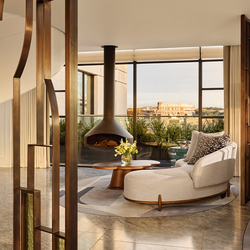 Lounge area with curved cream chaise, hanging fireplace, round coffee table, and views across the city from a spacious terrace.