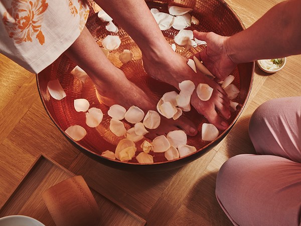 Presentation of spa treatments for the feet, which are in a basin with rose petals in a soothing and warm atmosphere.