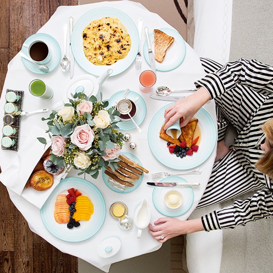 A hearty breakfast with smoothies, coffee, fruit, and pastries on the table, with a person putting toppings on the toast.