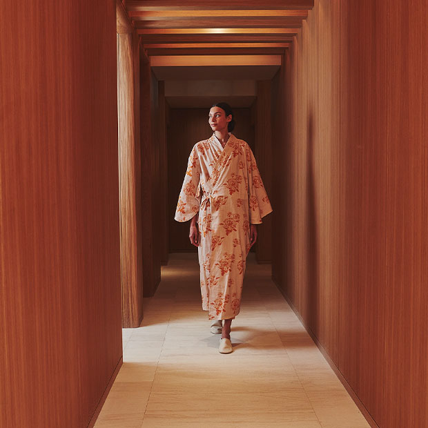 Woman in a patterned robe walking down a warm wood-paneled corridor in the spa.