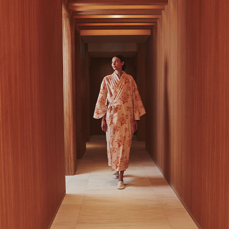 Woman in a patterned robe walking down a warm wood-paneled corridor in the spa.