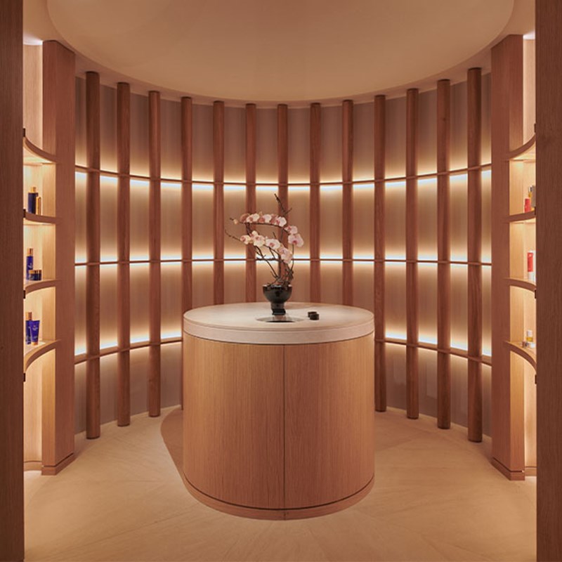 Curved wood-paneled spa retail space with softly lit shelves and a central display counter.