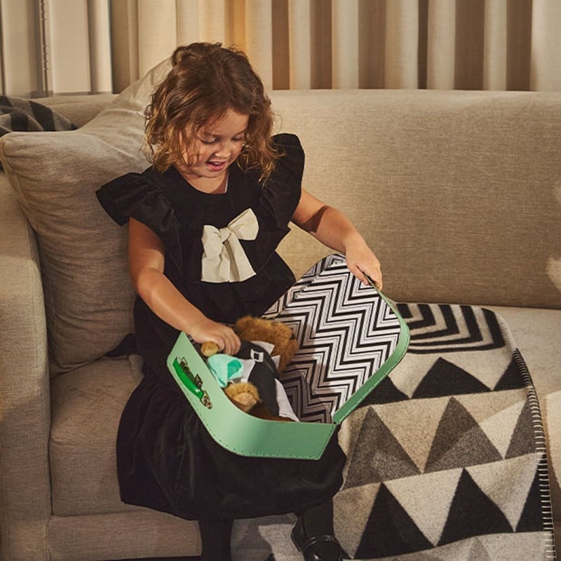 A young girl in a black dress with a large bow opens a Claridge’s green gift box to find a teddy bear inside.