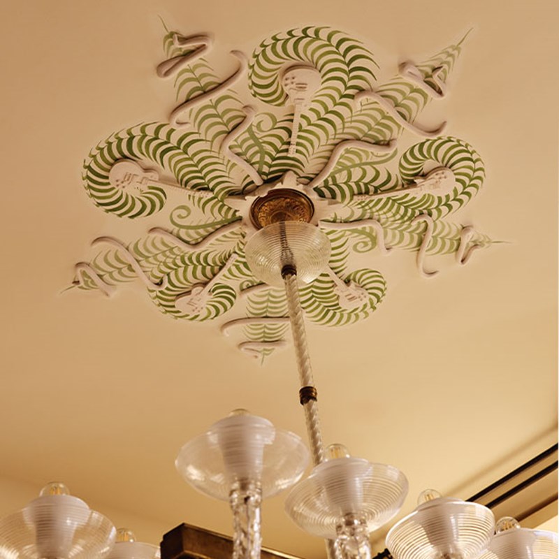 Decorative ceiling rose painted in green and white patterns with a glass chandelier suspended below.