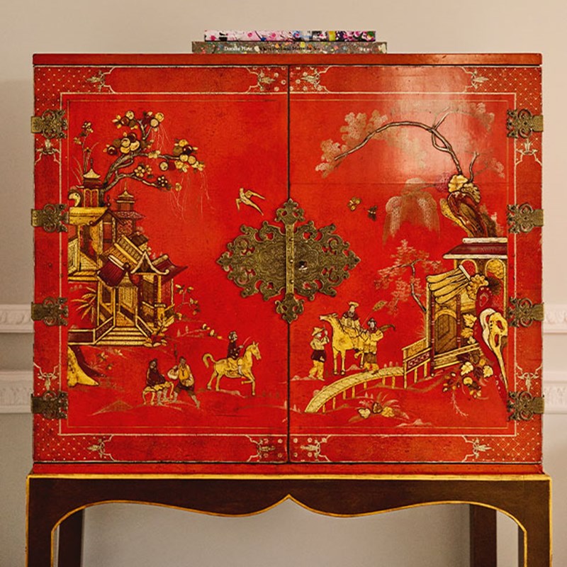 Red lacquered cabinet decorated with golden and painted scenes of figures, animals, and pagodas.