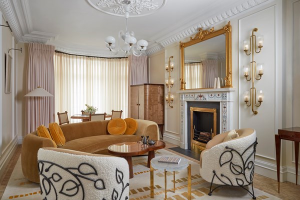 Elegant living room with curved velvet sofa, two patterned armchairs, ornate fireplace, and gold-framed mirror.