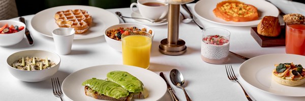 white table cloth and a selection of breakfast dishes including avocado on toast, Clardige's waffles, chia pudding and orange juice