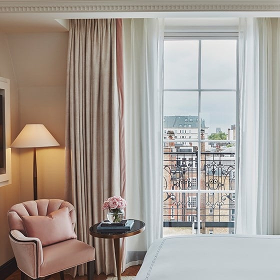 A pink armchair next to a table with a flower arrangement near the terrace in one of the bedrooms from Claridge's Hotel.