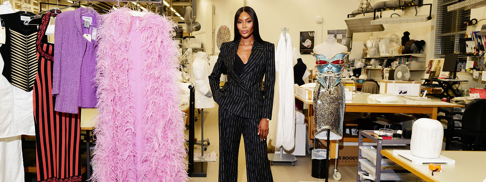 Naomi in black pin striped suit in atelier with dresses