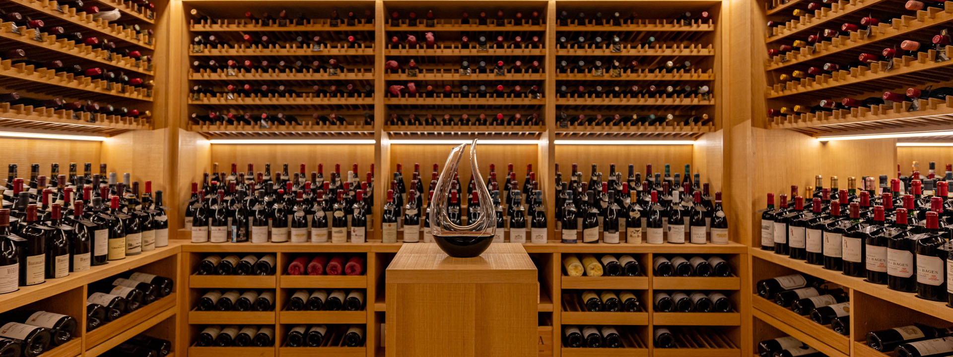 A collection of wine and champagne in the background, with a decanter in the middle at Claridge's Wine Cellar.