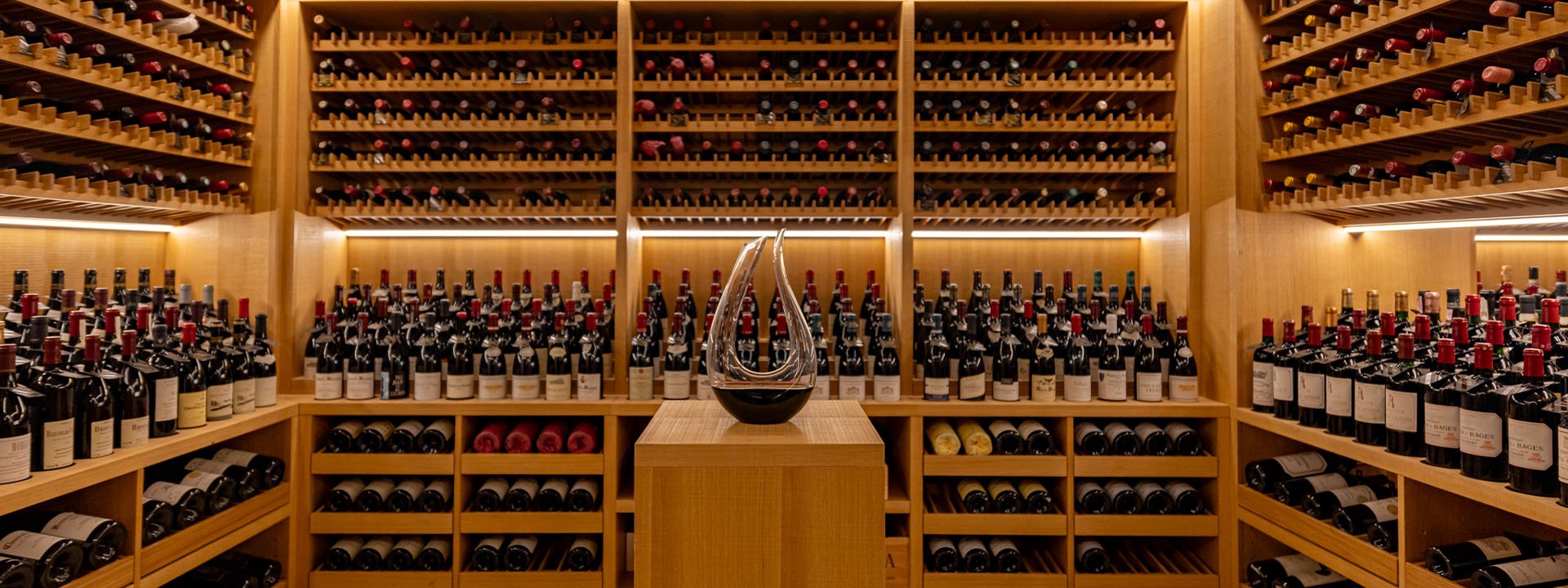 A collection of wine and champagne in the background, with a decanter in the middle at Claridge's Wine Cellar.